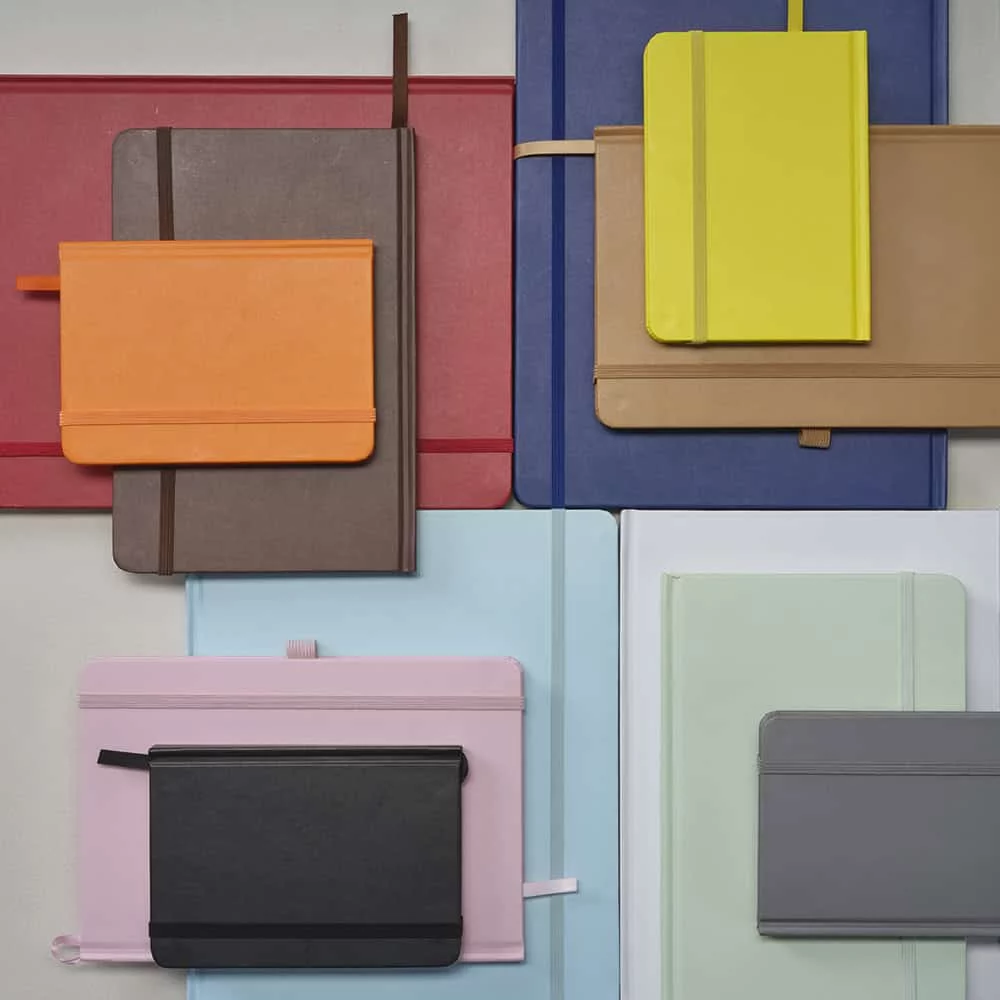 Collection de carnets et cahiers de différentes couleurs et tailles avec elastiques et rubans de fermeture, arrangés sur des supports colorés