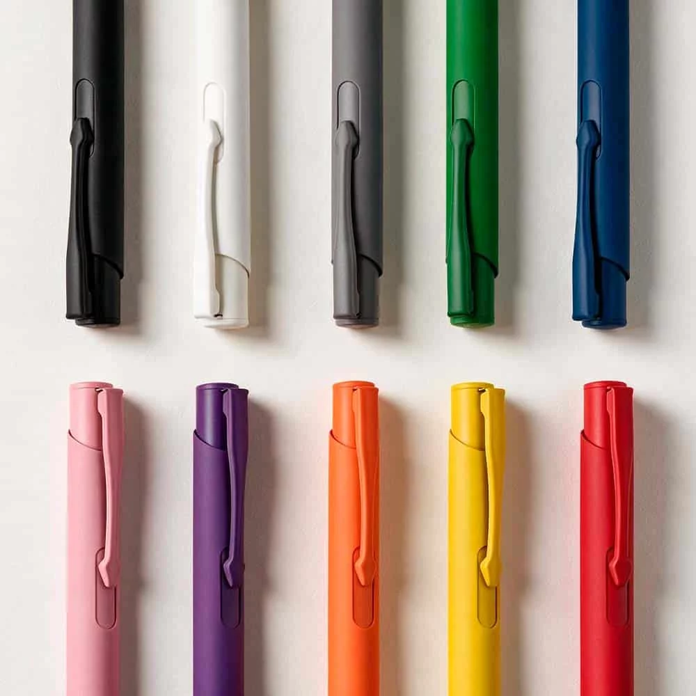 Dix stylos de différentes couleurs disposés en deux rangées sur un fond blanc : noir, blanc, gris, vert, bleu dans la rangée supérieure, et rose, violet, orange, jaune, rouge dans la rangée inférieure.