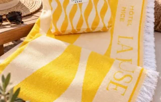 Serviettes de plage La Pérouse jaunes Serviettes de plage jaunes et blanches avec logo La Pérouse disposées sur une chaise longue face à la mer