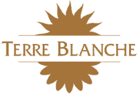 Logo Terre Blanche avec deux motifs floraux stylisés encadrant le texte en lettres dorées